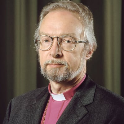 Biskop Juha Pihkala ser rakt in i kameran. Han bär en svart kavaj och prästkrage.