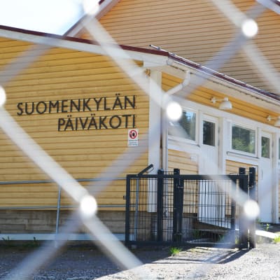 Ett gult trähus bakom ett stängsel. Det står Suomenkylän päiväkoti på väggen.