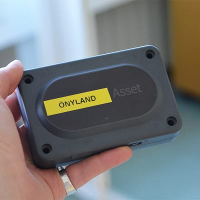 En hand håller i en fyrkantig svart plastdosa. På dosan står det önyland.