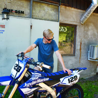 En ung man håller i en blå motorcykel.