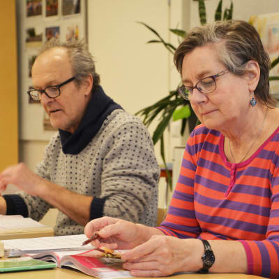 En kvinna och en man sitter bakom pulpeter och jobbar med läroböckerna framför sig.