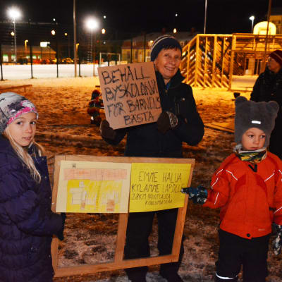 Flera vuxna och barn står utomhus och håller i skyltar. På en skylt står det behåll byskolan för barnens bästa.