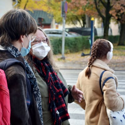 Två personer står och talar på gatan, båda har munskydd på sig.