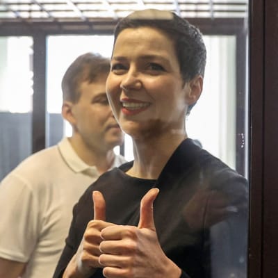 Miaria Kolesnikova visar tummen upp-tecken under rättegången mot henne. I bakgrunden står hennes medåtalade Maxim Znak.