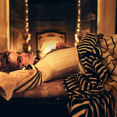 Emma Stones rollgestalt i The Favourite ligger i en utmanande ställning på en säng.
