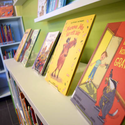 Färggranna barnböcker på flera hyllor i ett bibliotek.