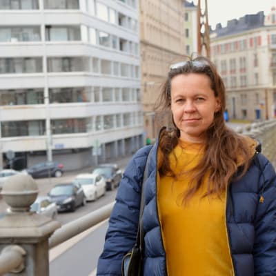 Pauliina Seppälä står på en väg vid ett räcke. Hon ser in i kameran, och det är mulet. Hon har på sig en blå jacka, och under det en gul ylletröja.