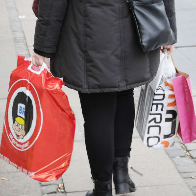Nainen kantaa muovikasseissa ostoksia.