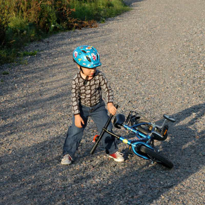 Lapsi nostaa kaatunutta polkupyörää soratiellä.