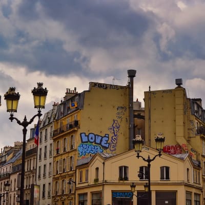 Korttelin päätytalot Pariisissa kahden tien risteyksessä, katulyhdyt talon päädyn molemmin puolin.