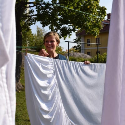 Daphne Jensen hänger upp vita lakan utanför ett gammalt, gult stenhus.