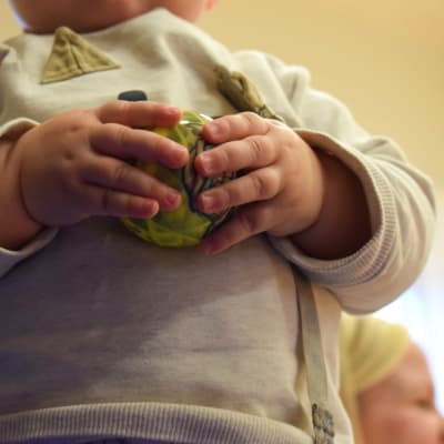 Två babyhänder som håller i en boll.