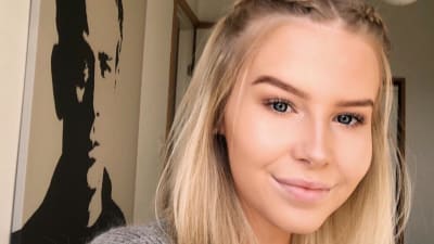 En ung kvinna med blont hår ser in i kameran och ler.