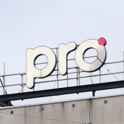 En skylt med texten "pro" ovanför på toggen av ett flervåningshus i stadsmiljö. 