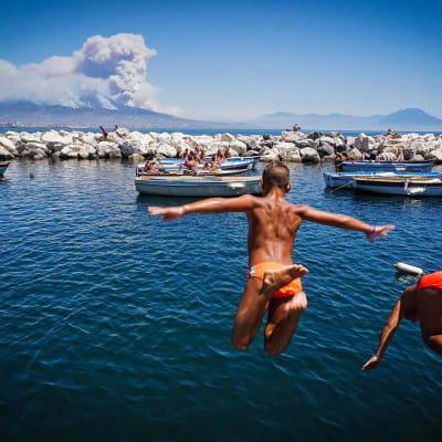 Napolilaislapset hyppivät uimaan samalla, kun Vesuviuksen ympärillä riehuvat metsäpalot savuttivat horisontin Italiassa 11. heinäkuuta.