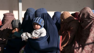 En grupp kvinnor iklädda burka och huvuddukar står i kö, vissa har barn i famnen.