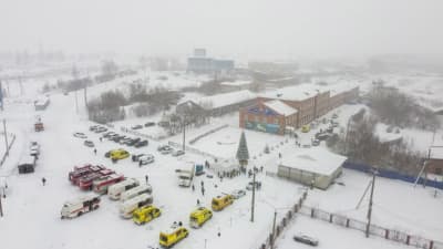 Ambulands och brandbilar står parkerade i ett snöigt landsskap bredvid flera långa tegelbyggnader