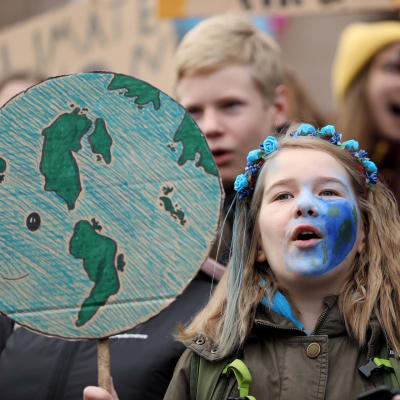 Unga demonstrerar för klimatet på riksdagshusets trappor i Helsingfors.