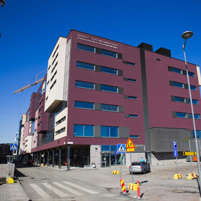 På bilden ser man ett stort vinrött hus. Huset är en hälsocentral.