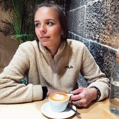 En kvinna sitter i ett kafé. Framför sig har hon en kopp kaffe.