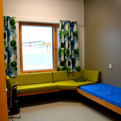ett rum med en grön soffa, gardiner med gröna detaljer, en säng med ett blått överdrag på