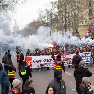 Mielenosoittajat marssivat banderollin kanssa kadulla Pariisissa ja polttavat hätäsoihtuja.