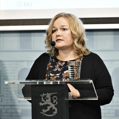 Omsorgsminister Krista Kiuru håller en presskonferens om reserestriktioner. Hon står vid ett talarpodium.