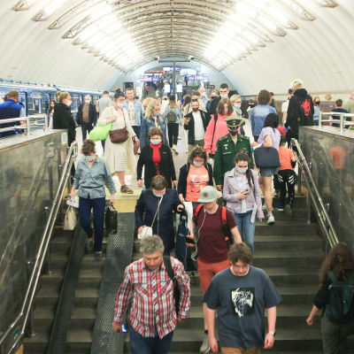 Människor går ner för trappan i S:t Petersburgs metro. De flesta bär munskydd.