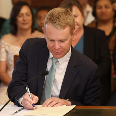 Uuden-Seelannin pääministeri Chris Hipkins allekirjoittaa asiakirjoja virkaanastujaisissaan. Taustalla näkyy tilaisuuden vieraita.