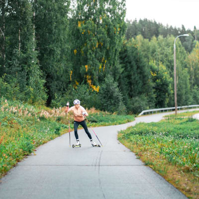 Kaisa Mäkäräinen rullahiihtää Kolin kansallispuistossa kevyen liikenteen väylällä. Väylän varrella syksyisiä ksaveja ja puita. 