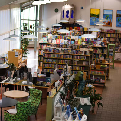 Nedre våningen i ett bibliotek med hyllor, bord och stolar.
