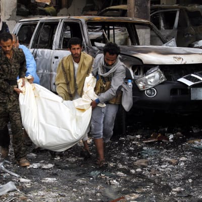 Yemeniläisiä miehiä kantamassa kuollutta henkilöä ulos raunioista.