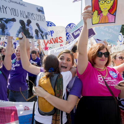 Joukko juhlivia ja halailevia naisia, naisilla on käsissään mielenosoitusjulisteita.