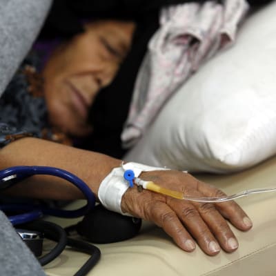 Vanhempi nainen nukkuu sairaalasängyssä, hänen käteensä on asetettu tippa.