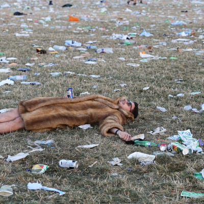 Mies makaa roskien peittämän Glastonburyn festivaalialueen nurmikolla festivaalin päätyttyä.