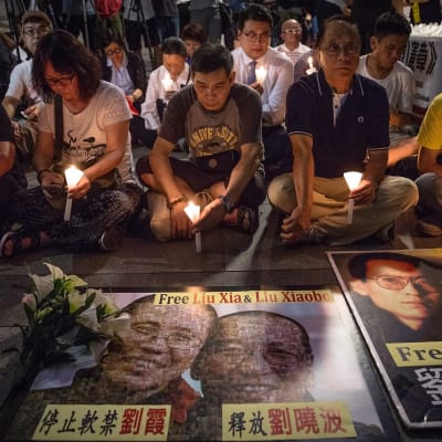 Ihmisiä istuu kynttilöiden kanssa, etualalla Liu Xiaobon ja hänen puolisonsa Liu Xian kuvat.