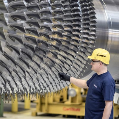 Siemensin työntekijä seisoo suuren turbiinin vieressä tehtaalla Berliinissä.
