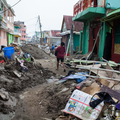 Tuhoja Dominican pääkaupungin kaduilla. Kadulla on hirmumyrskyn ympäriinsä heittelemää romua. Nainen kävelee kadulla kantaen jotain.
