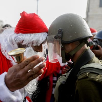 Israelilainen sotilas ja joulupukiksi pukeutunut palestiinalainen mielenosoittaja ottavat mittaa toisistaan otsa otsaa vasten.