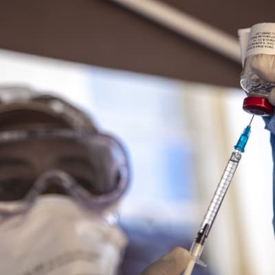 Ebolaa vastaan suojautunut terveydenhuollon työntekijä ottaa rokotetta rokotuspiikkiin pullosta.