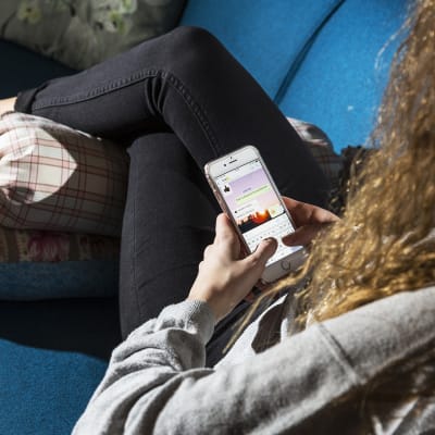 Nuori suomalainen nainen istuu sohvalla ja käyttää Snapchattia.