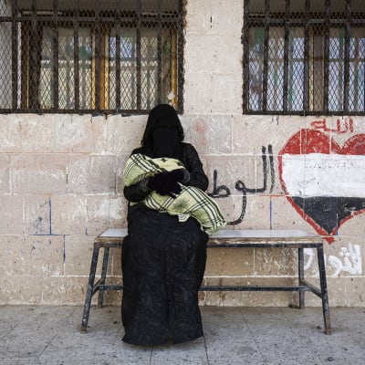 Jemeniläinen burkaan pukeutunut nainen vauva sylissään odottaa ruoka-apua.