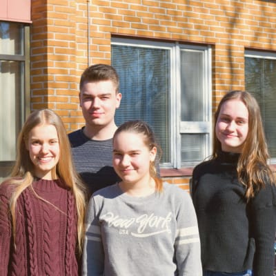 Fyra gymnasieelever ståt ute på en skolgård.