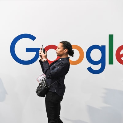 Nainen ottamassa selfietä.  Taustalla olevalla valkoisella seinällä on Googlen logo.