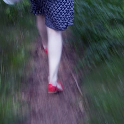 nainen juoksee polulla punaisissa kengissään