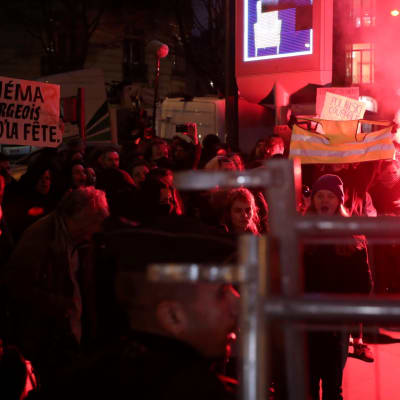 Mielenosoittajia kylttien ja soihtujen kanssa Salle Pleyel -salin edessä.