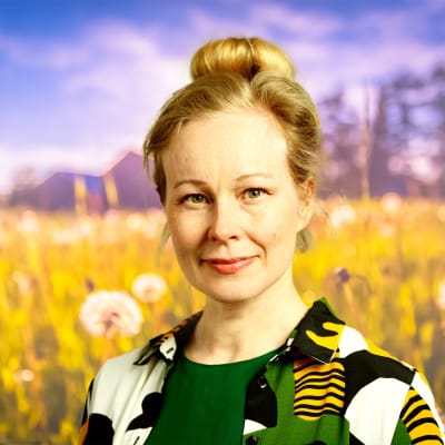 Aja Lund ser rakt in i kameran med ett litet leende med en sommaräng i bakgrunden.