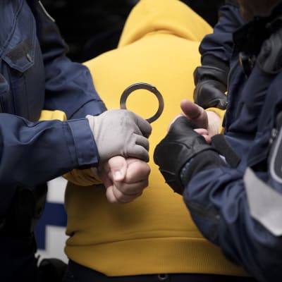 Poliisit laittavat käsirautoja pidätetyn käsiin.