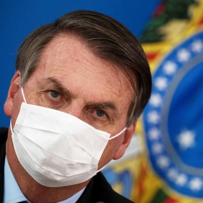 Brasiliens president Jair Bolsonaro med ansiktsskydd på sig. Brasiliens flagga syns till höger om honom.