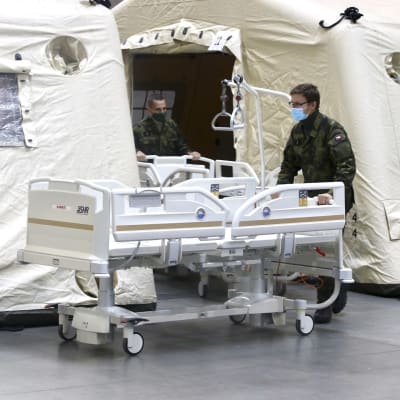 Sotilaat siirtävät sairaalasänkyä telttamaiseen rakennukseen.